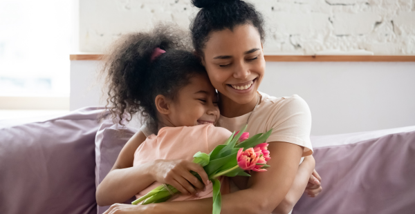 Une femme embrasse son enfant tout en tenant un bouquet de tulipes.