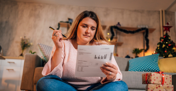 Une femme examine son budget dans un salon décoré aux couleurs des fêtes de fin d'année.