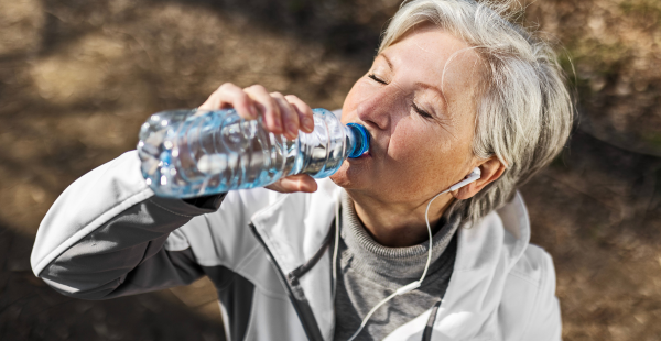 Une femme appréciant d'être dehors dans un paysage automnal, buvant d'une bouteille d'eau.