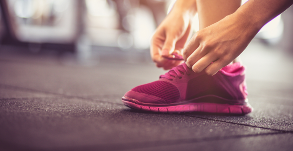 A pair of hands tying the laces on a pink running shoe.